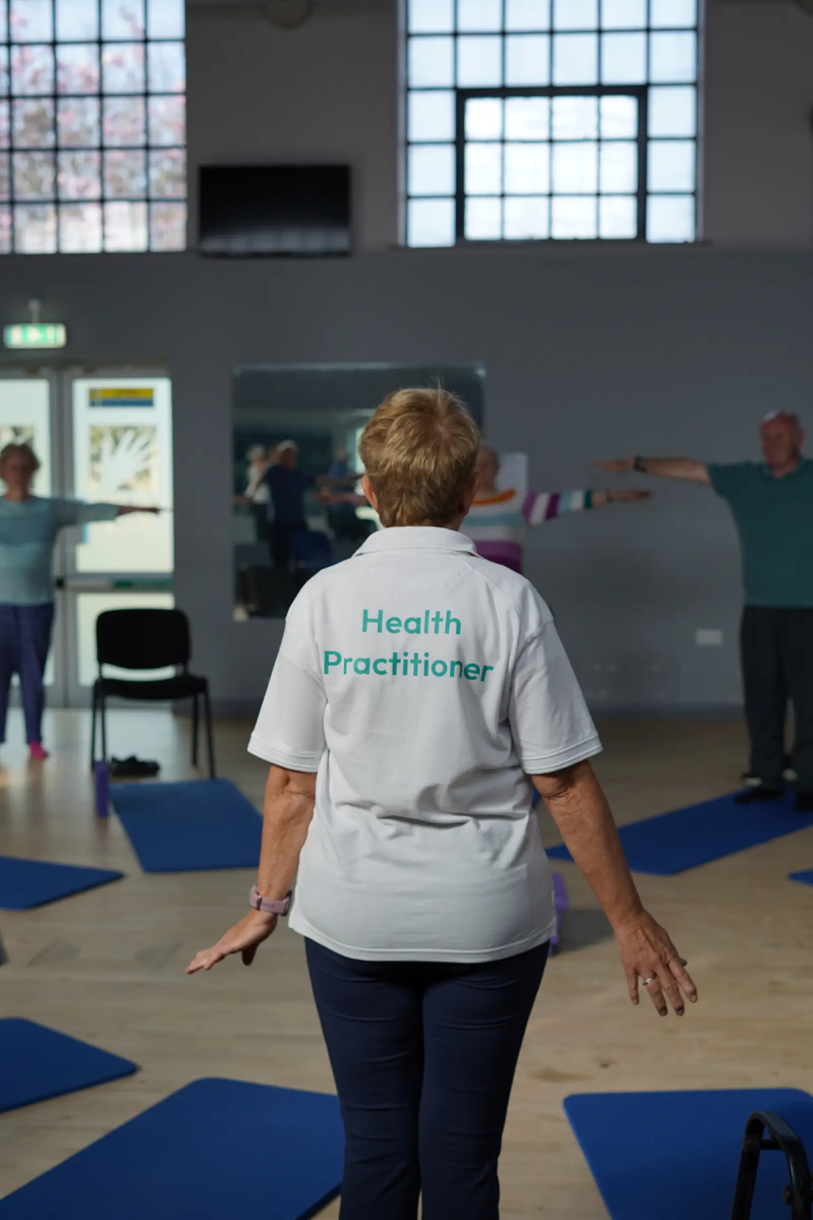 A lady wearing a health practitioner t shirt, taking a mobility class